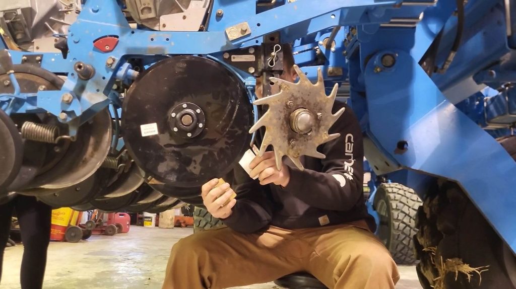 Mechanic adjusting seed disc openers in a workshop, demonstrating maintenance and quality check procedures