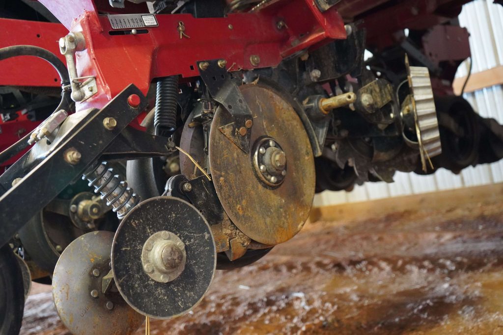 Close-up of red seed disc opener assembly on a farm planter, showing detailed components and wear signs.