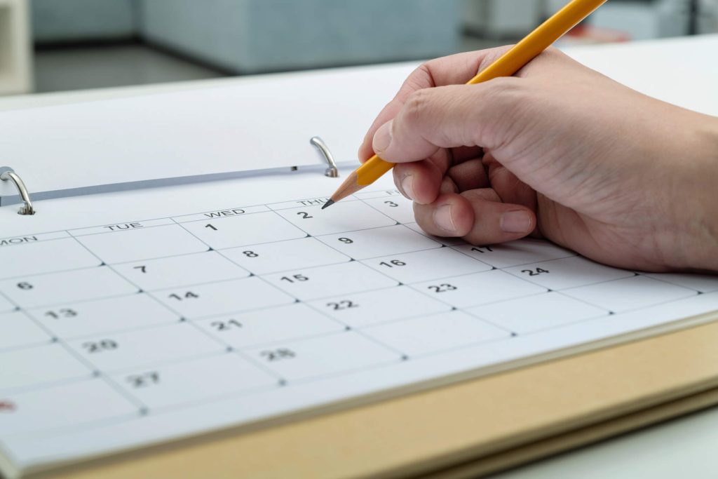Hand marking dates on a calendar for tracking last frost and optimal planting time