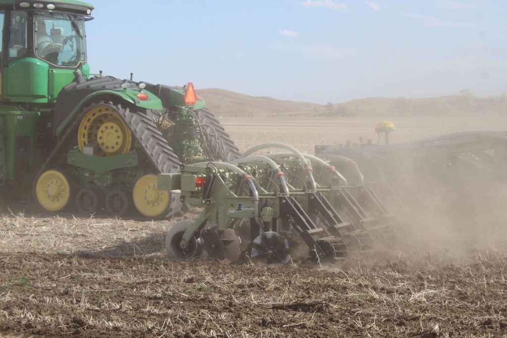 Tractor using strip-till machinery in a dusty field during early spring field prep.